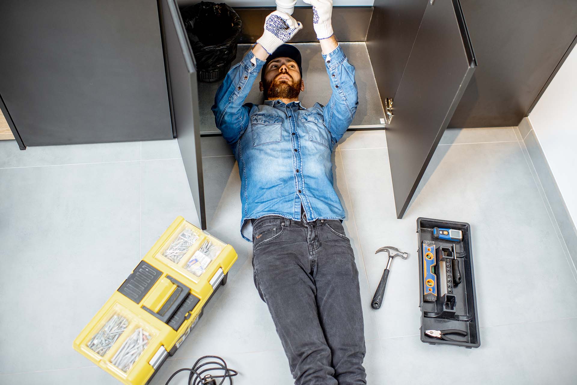 A man working on the pipes under the sink in a modern kitchen.