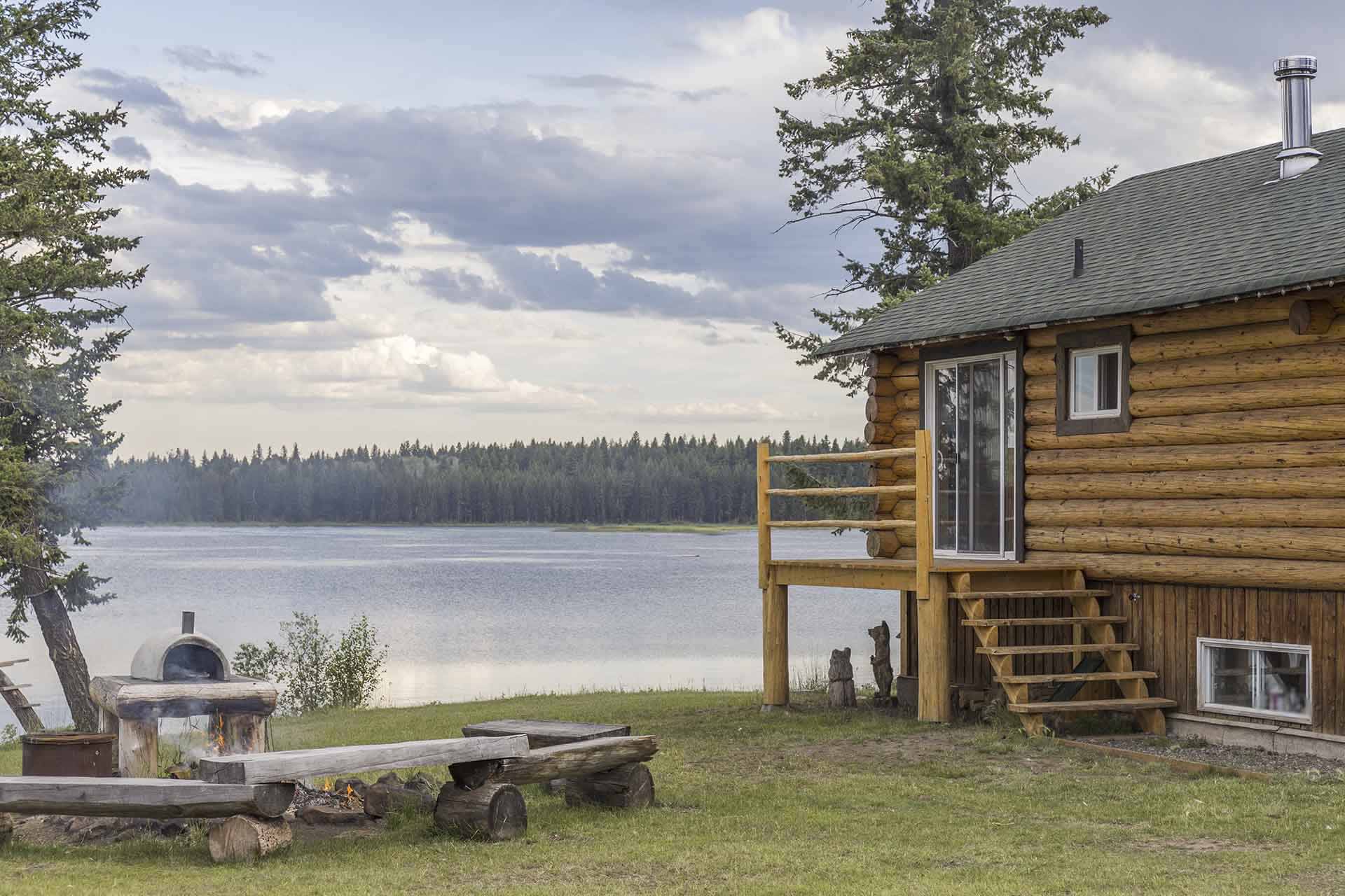 A log cabin on a lake with a porch and a picnic area.